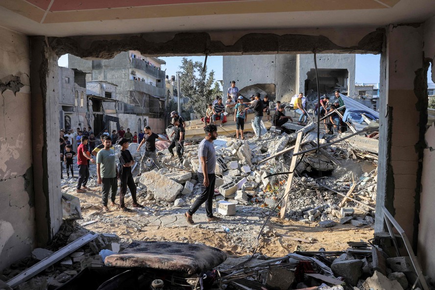 Pessoas se reúnem perto dos escombros de um prédio após um ataque aéreo israelense em Rafah, no sul da Faixa de Gaza,