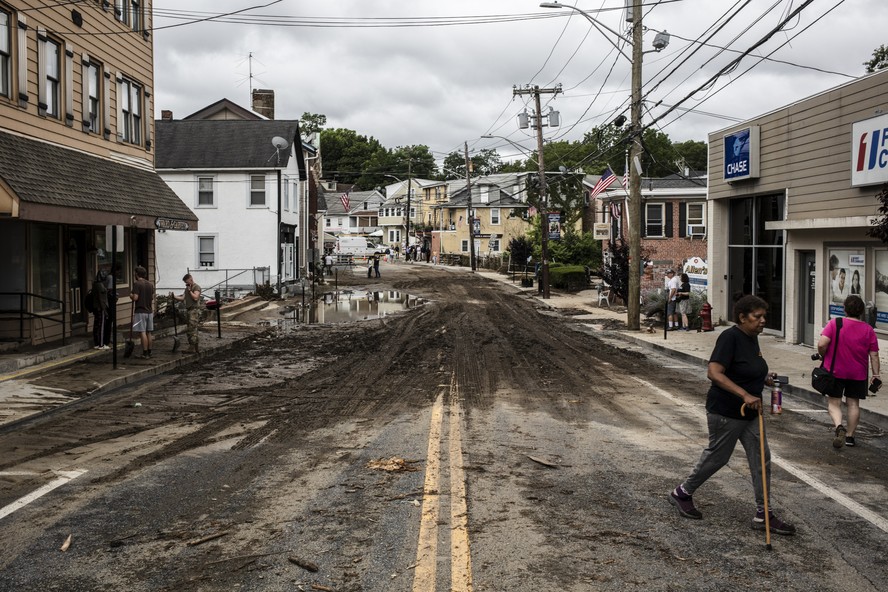 Mulher caminha em rua com asfalto destruído após enchente em Nova York