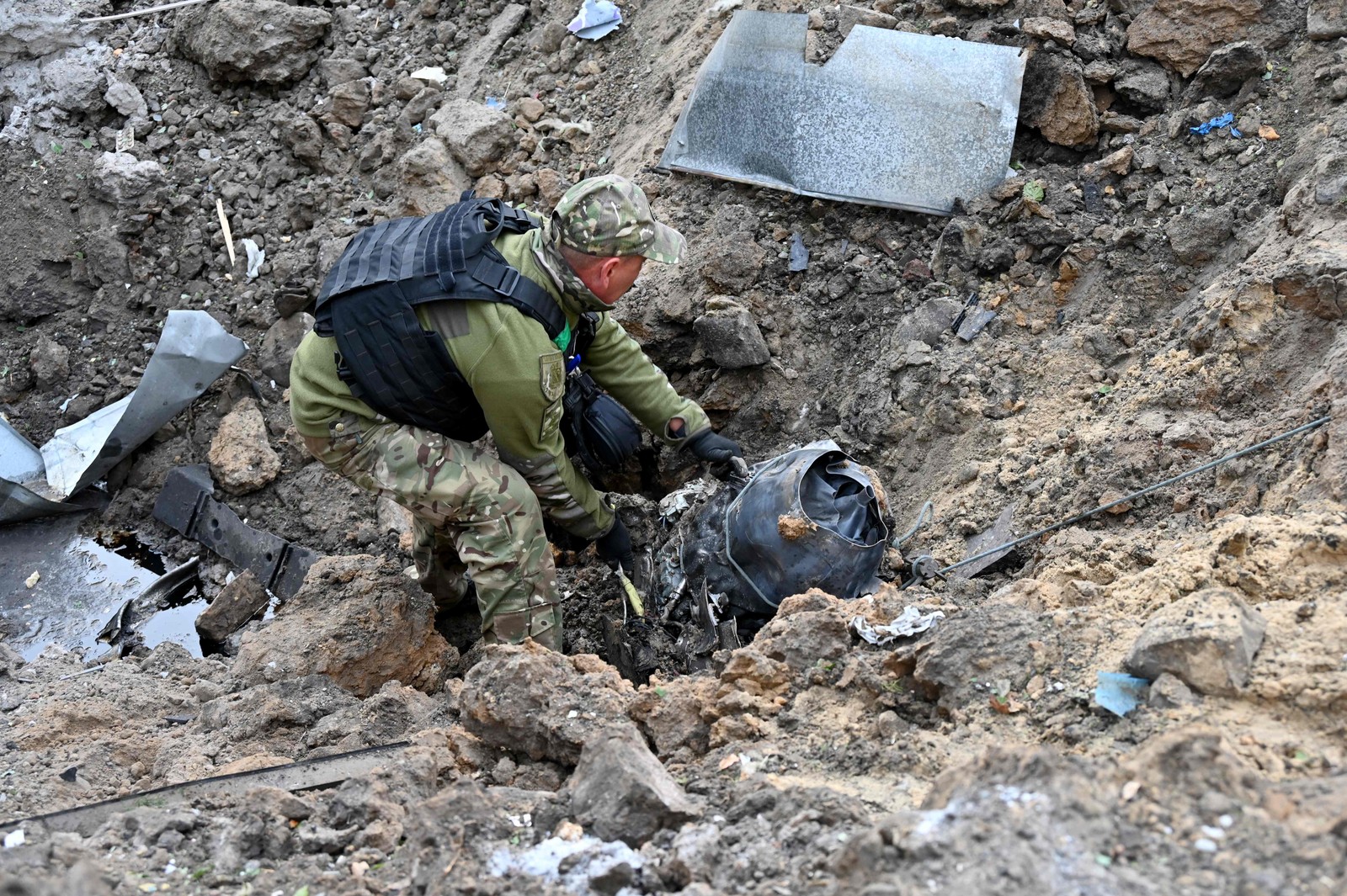 Uma equipe de resgate move um fragmento de um míssil de uma cratera após ataque russo para o centro da cidade ucraniana de Kharkiv — Foto: SERGEY BOBOK / AFP