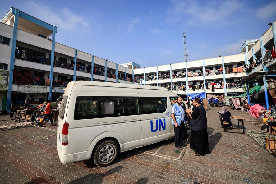 Um homem fala com um funcionário da Agência das Nações Unidas de Assistência e Obras para os Refugiados da Palestina (UNRWA) do lado de fora de um de seus veículos estacionados no playground de uma escola administrada pela UNRWA que foi convertida em um abrigo para palestinos deslocados em Khan Yunis, em no sul da Faixa de Gaza