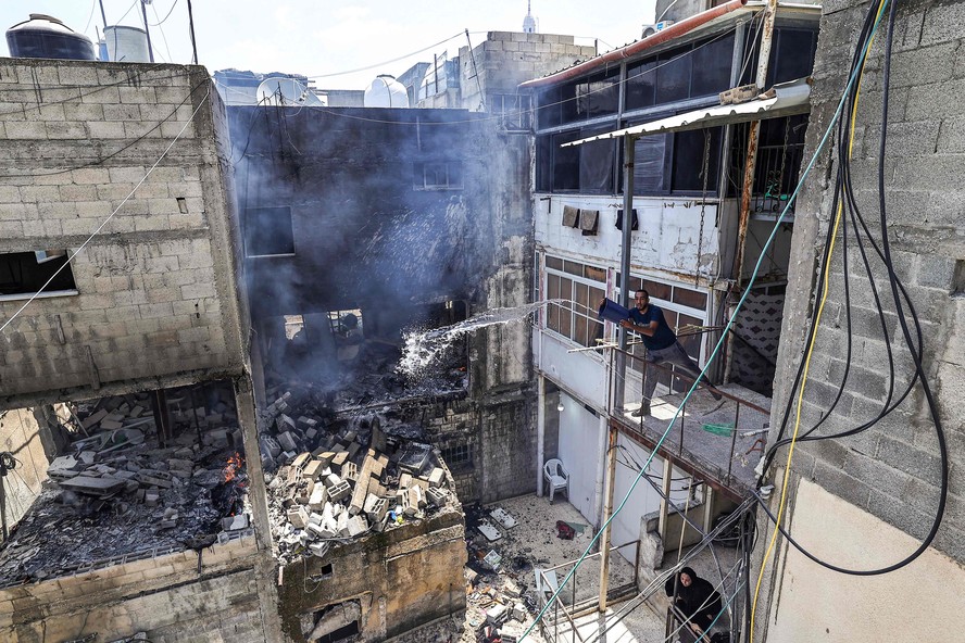 Morador tenta apagar incêndio em um prédio atingido pelo Exército israelense no campo de refugiados palestinos de Nur Shams