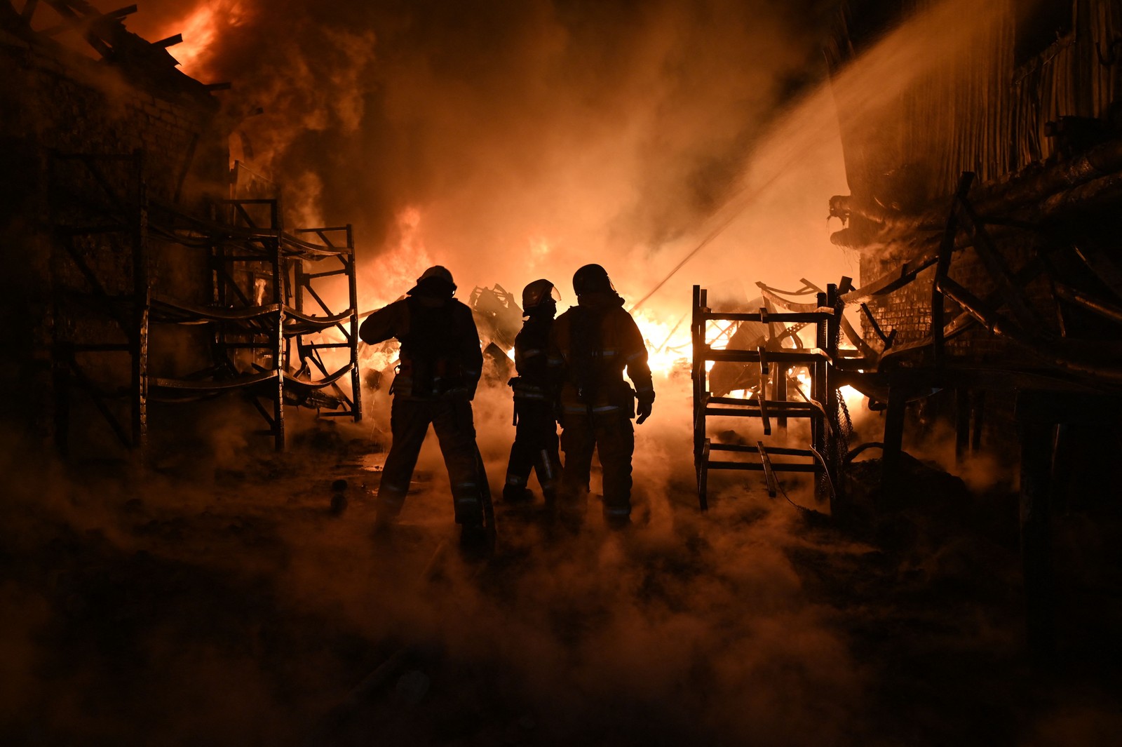 Bombeiros ucranianos trabalham para extinguir um incêndio no local de um ataque de drones a instalações industriais em Kharkiv — Foto: SERGEY BOBOK/AFP