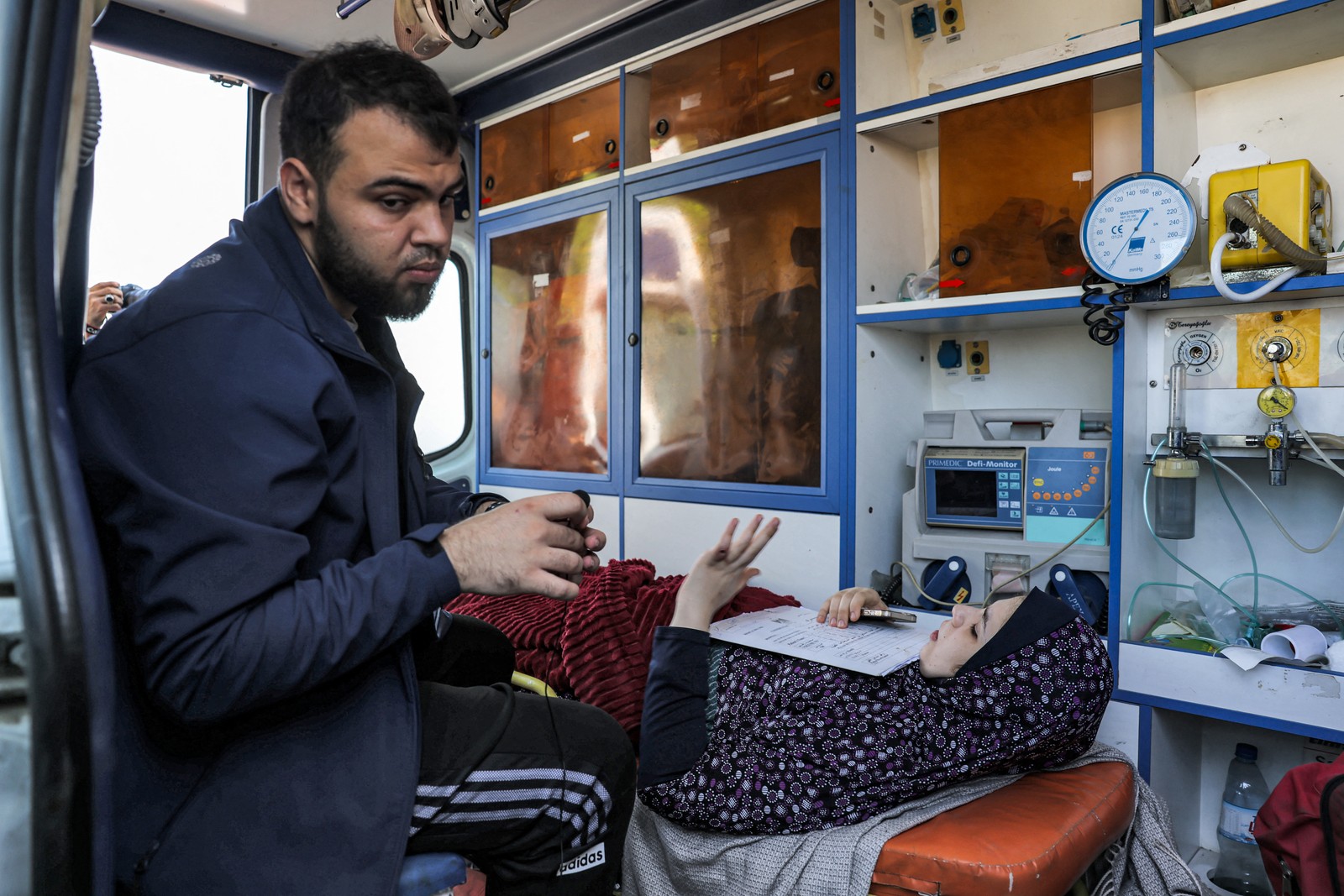 Uma jovem deita-se com papéis e um telefone dentro de uma ambulância esperando na passagem de fronteira de Rafah, no sul da Faixa de Gaza, antes de receber cuidados médicos no Egito — Foto: Mohammed ABED/AFP