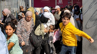 Pessoas atravessam um portão para entrar na passagem de fronteira de Rafah para o Egito, no sul da Faixa de Gaza — Foto: Mohammed ABED/AFP