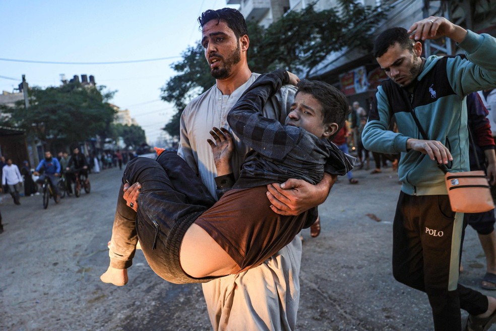 Palestino ajuda jovem ferido em ataque israelense em Rafah, no sul da Faixa de Gaza — Foto: SAID KHATIB / AFP