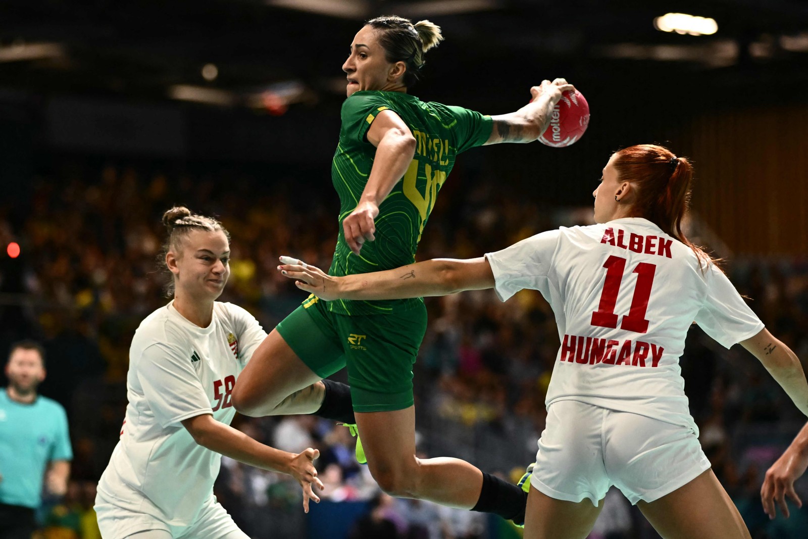 A zagueira brasileira Patricia Matieli tenta marcar um gol contra a pivô húngara Reka Bordas e a lateral direita húngaraAnna Albek durante a partida de handebol do Grupo B — Foto: Aris MESSINIS / AFP