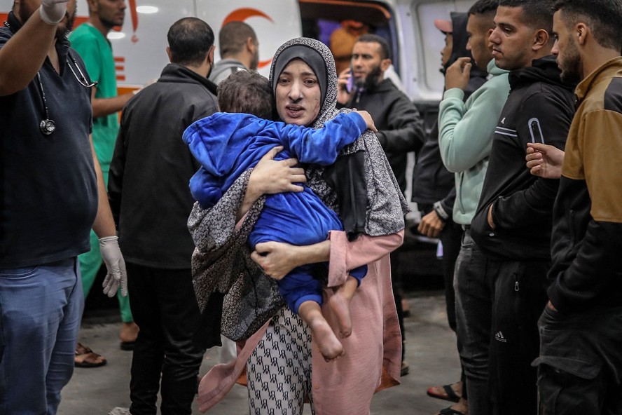 Mulher palestina coberta de poeira corre com seu filho nos braços para o hospital Hospital al-Shifa, o maior de Gaza, após o bombardeio israelense em Khan Yunis, no sul da região, em 15 de novembro de 2023