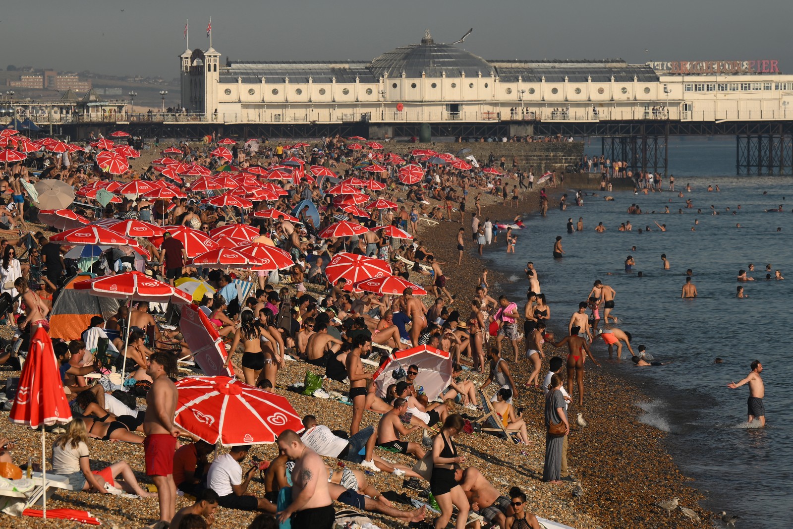 Banhistas são vistos aproveitando o sol e o mar na praia de Brighton — Foto: AFP