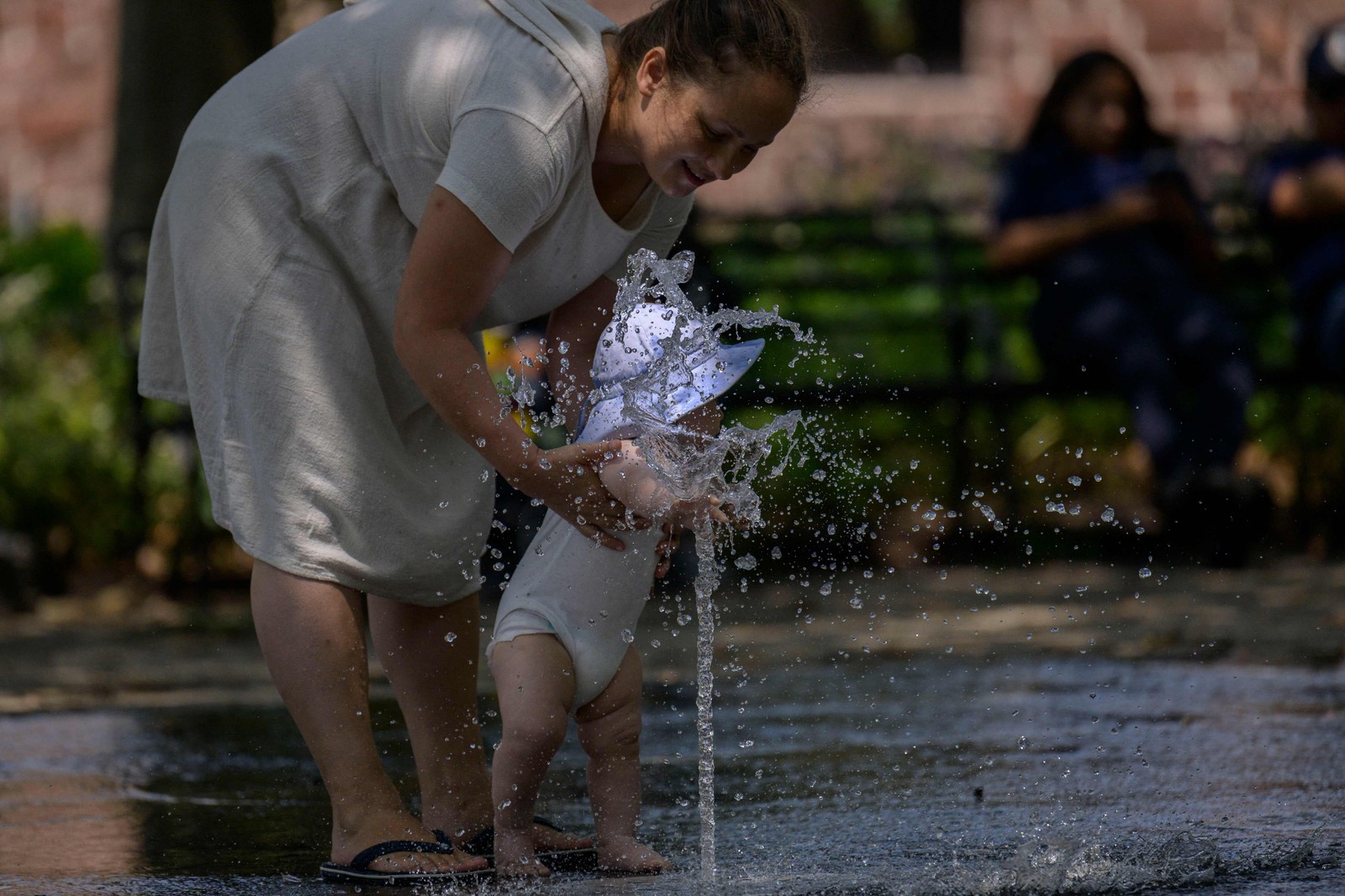 Mulher e seu bebê se refrescam em uma fonte pública em um parque em Nova York, em 26 de julho de 2023 — Foto: ANGELA WEISS / AFP
