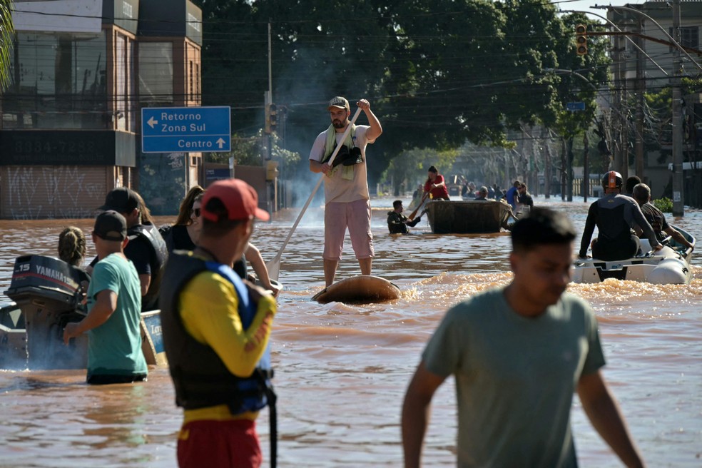 Em Porto Alegre, homem passa com prancha enquanto equipes de resgate vasculham prédios. — Foto: Nelson Almeida/AFP