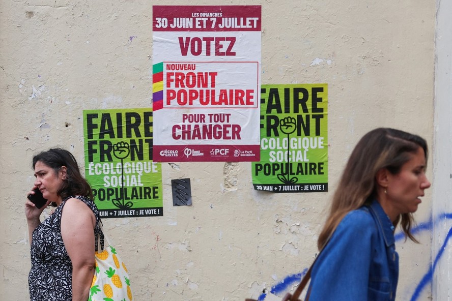 Franceses caminham em frente à cartaz eleitoral na França