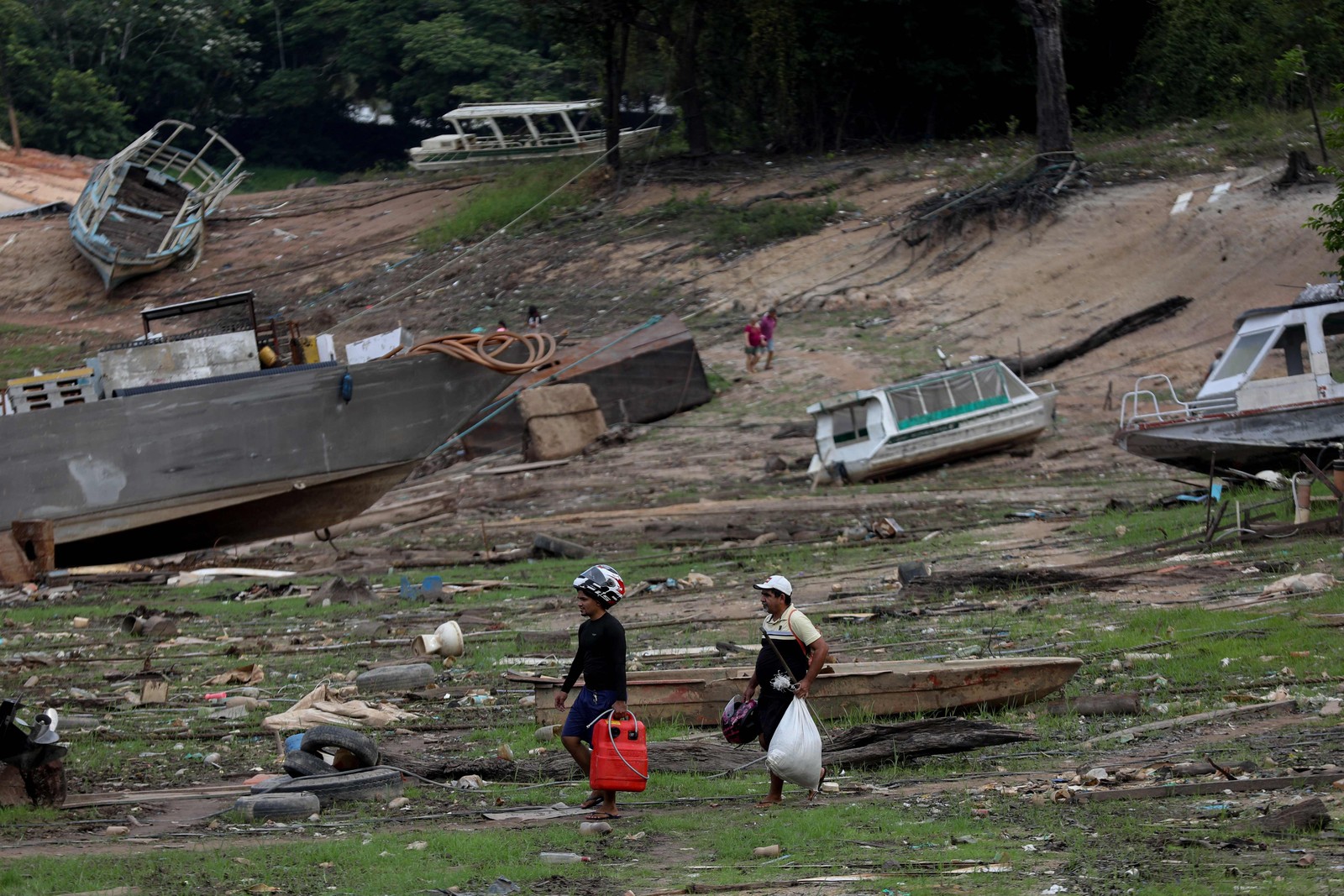 Pessoas caminham entre barcos encalhados no Rio Negro durante a seca — Foto: Michael Dantas/AFP