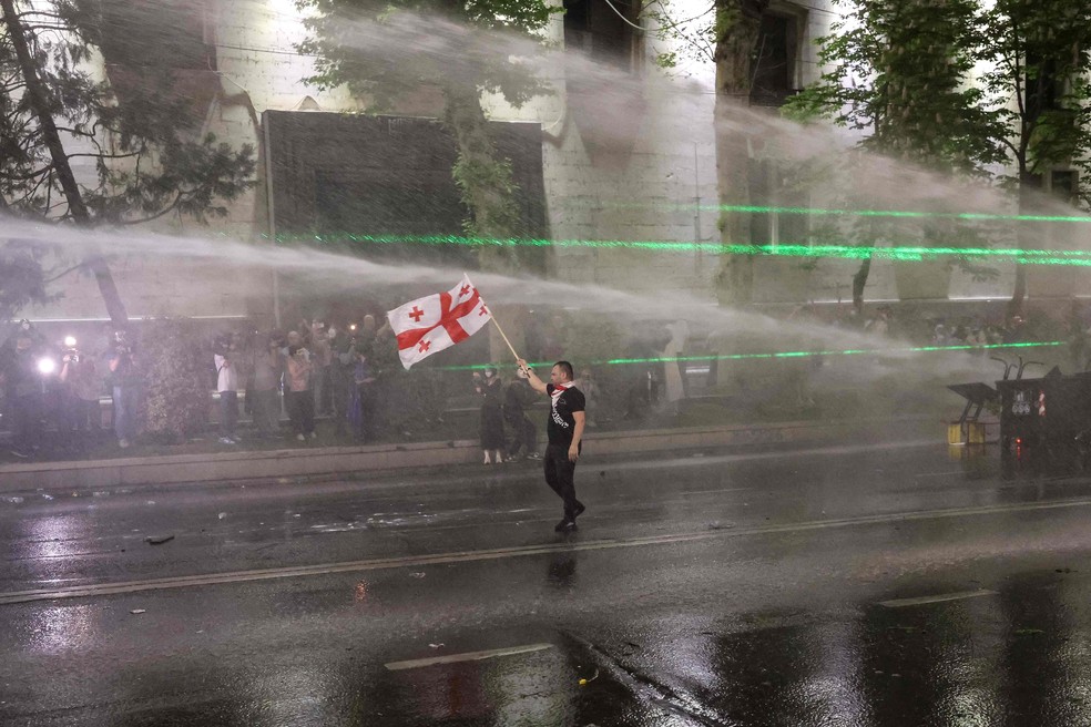 Manifestante ergue bandeira da Geórgia enquanto polícia atira jatos de água para dispersar ato — Foto: Giorgi Arjevanidze/AFP
