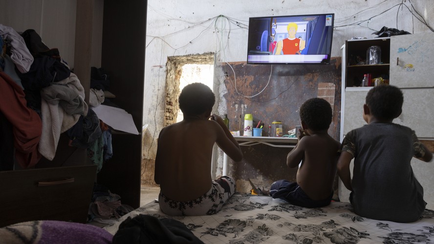 Crianças assistem TV em casebre numa comunidade carioca