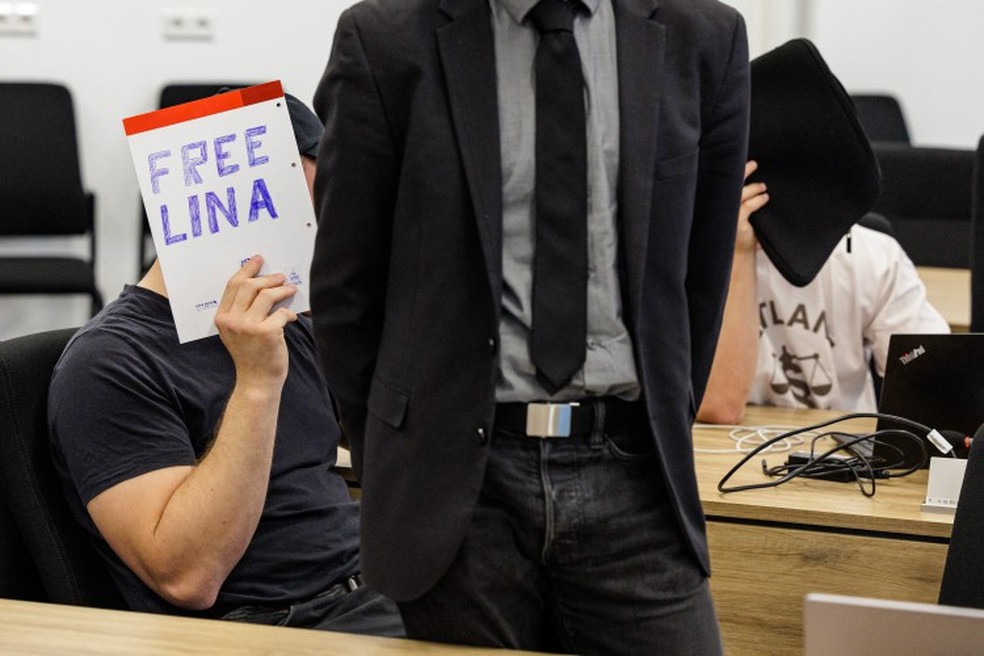 Um réu esconde o rosto atrás de um papel com a inscrição 'Libertem Lina' no tribunal no tribunal regional em Dresden, Alemanha — Foto: Jens Schlueter / AFP