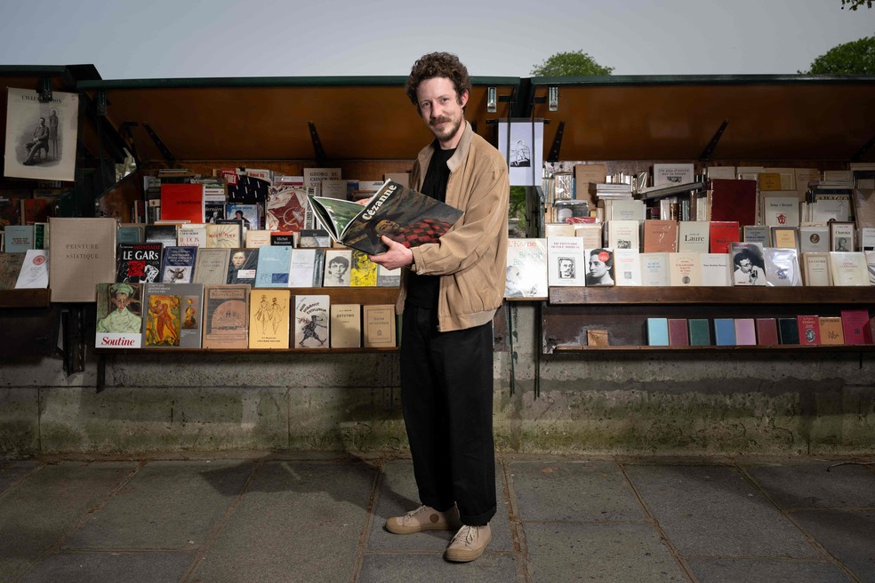 O vendedor de livros usados ('bouquiniste') Edouard posa em frente a sua banca às margens do Rio Sena, em Paris — Foto: Miguel Medina / AFP