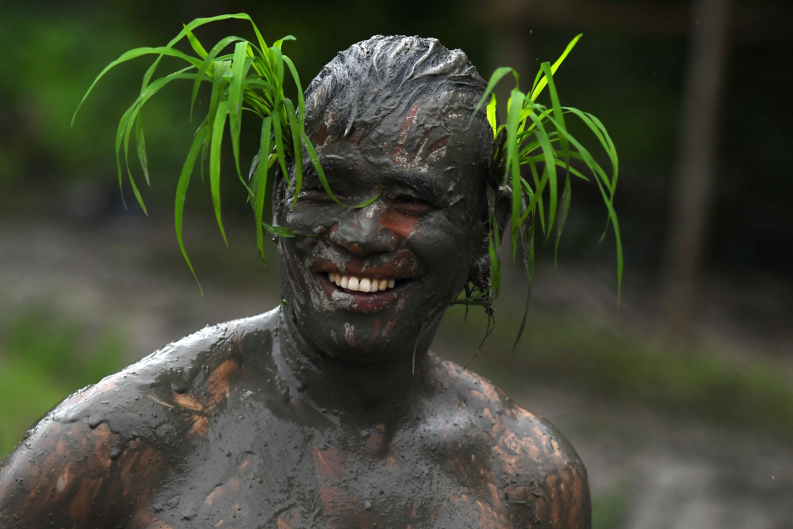 Agricultor coberto de lama com mudas de arroz na cabeça sorri em um arrozal durante o "Dia Nacional do Arroz", que marca o início da temporada anual de plantio de arroz, na vila de Tokha, nos arredores de Katmandu, Nepal  — Foto: PRAKASH MATHEMA / AFP