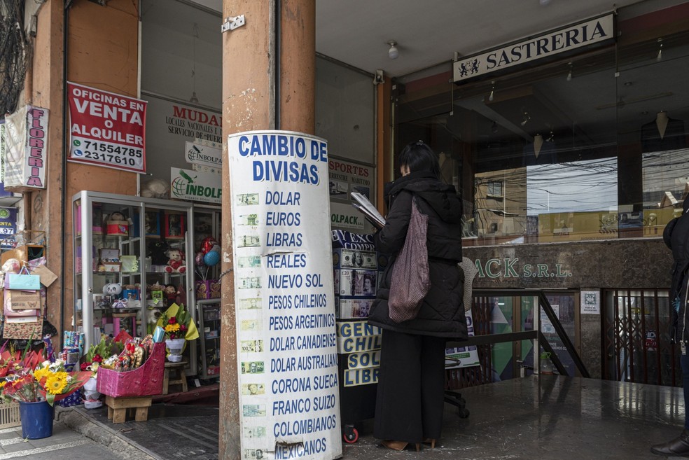 Cliente em uma casa de câmbio de La Paz, onde um cartaz mostra as diferentes moedas oferecidas para troca — Foto: Marcelo Perez del Carpio/Bloomberg
