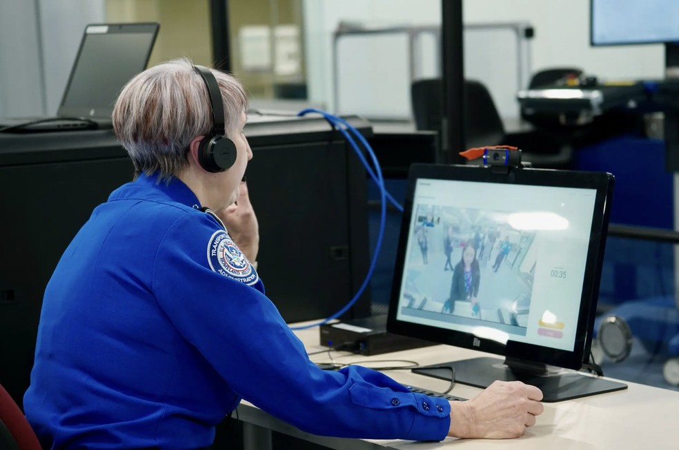 Um oficial da TSA, trabalhando remotamente, ajuda um viajante usando um monitor de vídeo — Foto: TSA no Aeroporto Internacional Harry Reid em Las Vegas via The New York Times