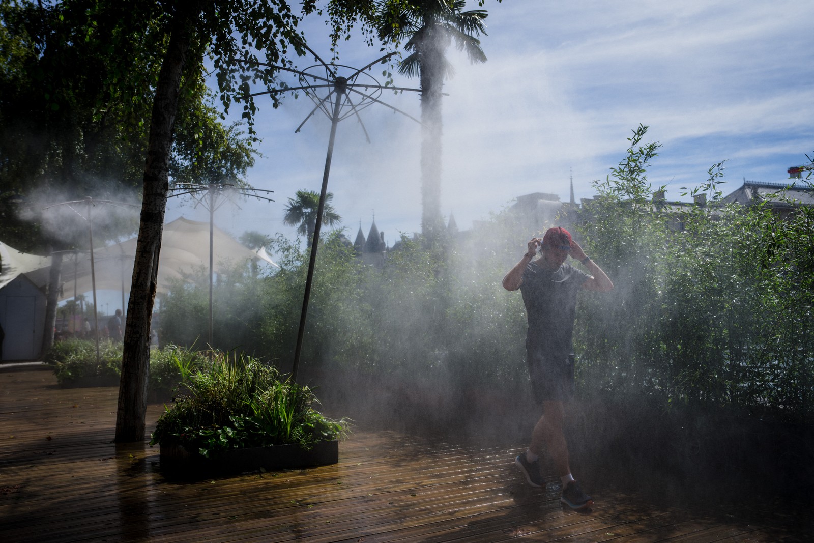 Um homem caminha sob uma máquina de neblina para se refrescar em uma margem do rio Sena, no centro de Paris — Foto: AFP