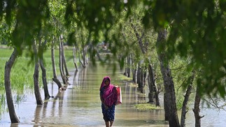 Mulher atravessa a maré entupida após o ciclone Sitrang atingir Kalapara, Bangladesh, onde centenas de milhares de pessoas foram evacuados de casa — Foto: MUNIR UZ ZAMAN/AFP