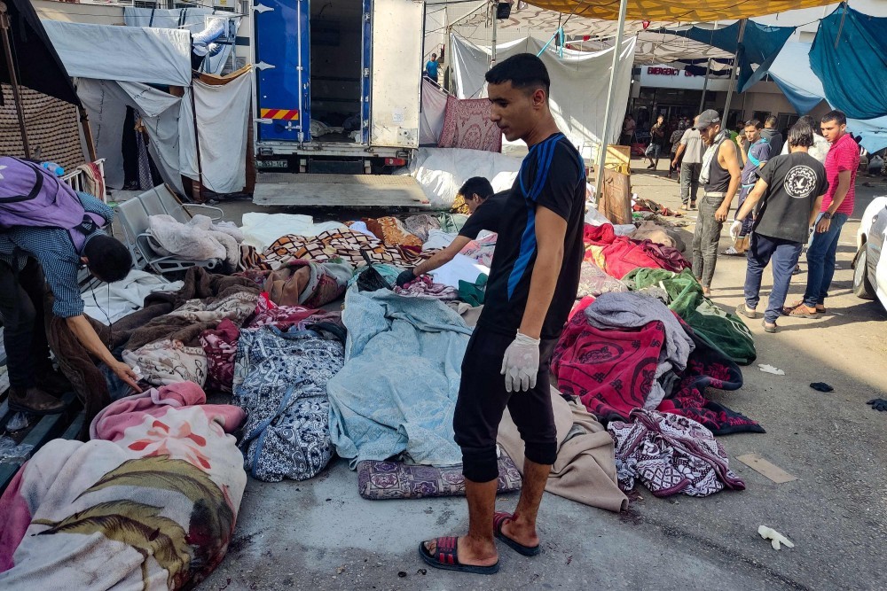 Homens verificam os corpos de pessoas mortas em um bombardeio que atingiu uma escola que abrigava palestinos desabrigados, enquanto eles jazem no chão no pátio do hospital Al-Shifa, na Cidade de Gaza — Foto: Khoder al-Zaanoun / AFP