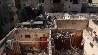 Um homem palestino descansa depois de encher um galão com água do telhado de uma casa fortemente danificada após o bombardeio israelense no distrito de Tal al-Sultan, em Rafah, no sul da Faixa de Gaza — Foto: AFP