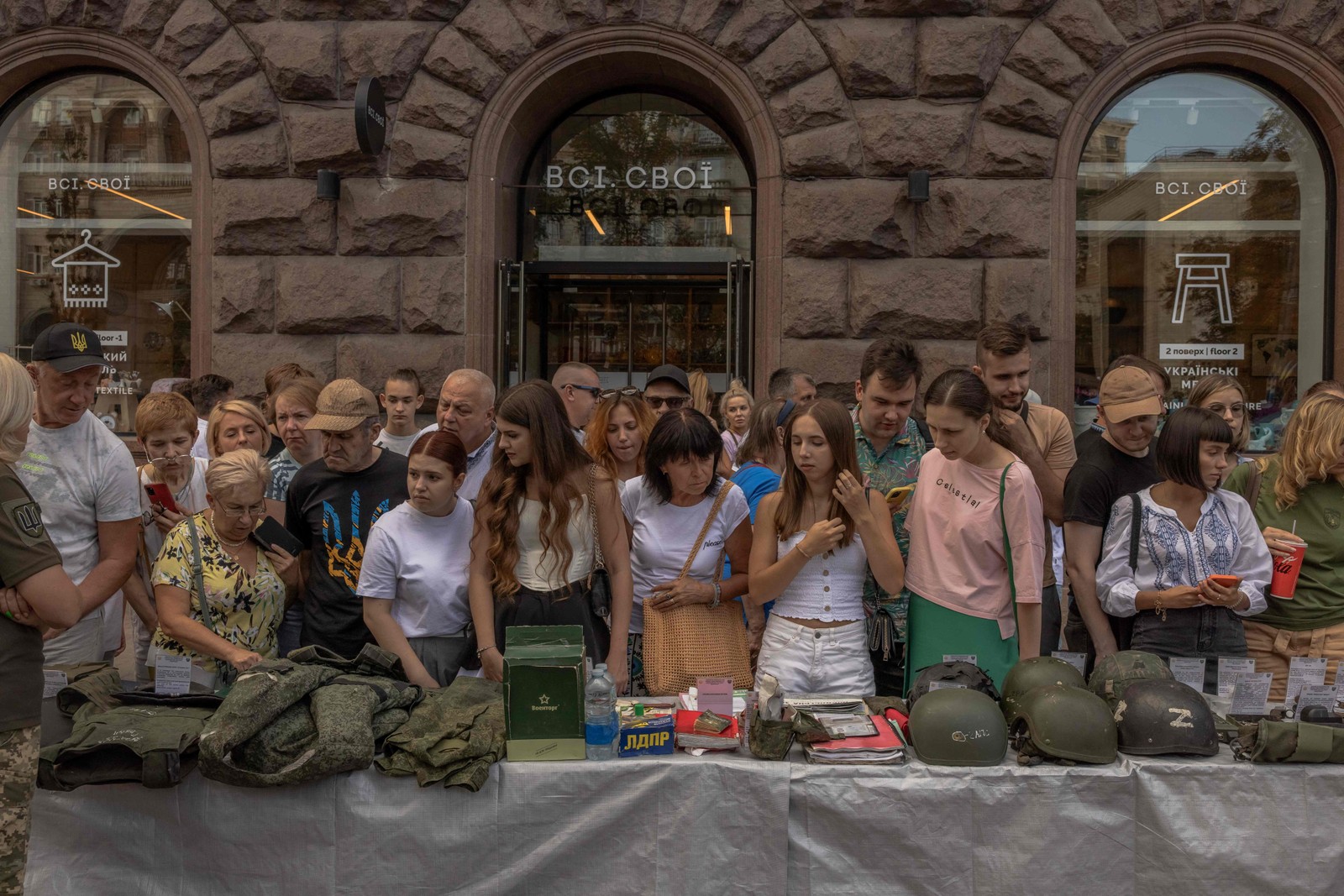 Pessoas observam uniformes militares russos, capacetes e outros itens que foram encontrados em campos de batalha. Material foi colocado em exibição na rua Khreshchatyk, no Dia da Independência da Ucrânia, em Kiev — Foto: Roman Pilipey / AFP