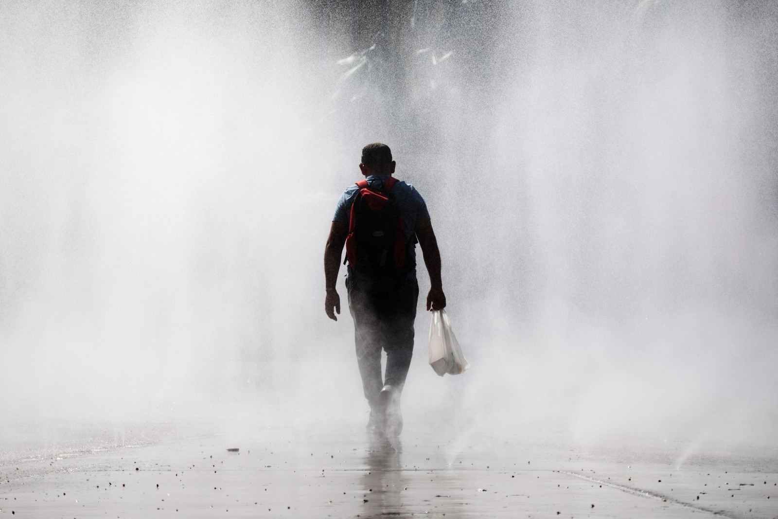 Homem atravessa um spray de água em frente à estação de trem Praterstern, em Viena, em 21 de agosto de 2023, onde a atual onda de calor mantém as temperaturas em torno de 35°C — Foto: Alex HALADA / AFP