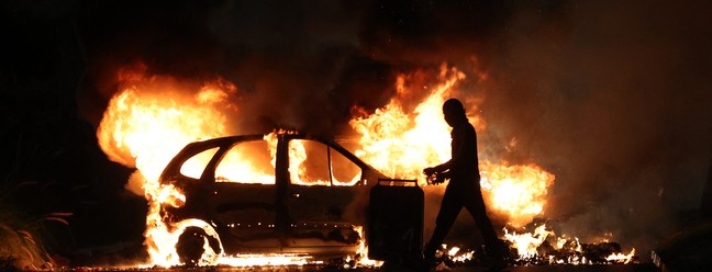 Manifestante caminha ao lado de um carro em chamas durante confrontos com a polícia em Le Port, ilha francesa de La Reunion, no Oceano Índico, em 30 de junho de 2023 — Foto: RICHARD BOUHET / AFP