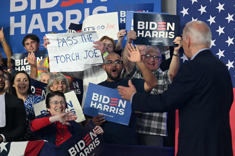 Presidente dos EUA, Joe Biden, acena a apoiadores antes de discurso no Wisconsin; um deles levanta cartaz dizendo 'passe o bastão', Joe