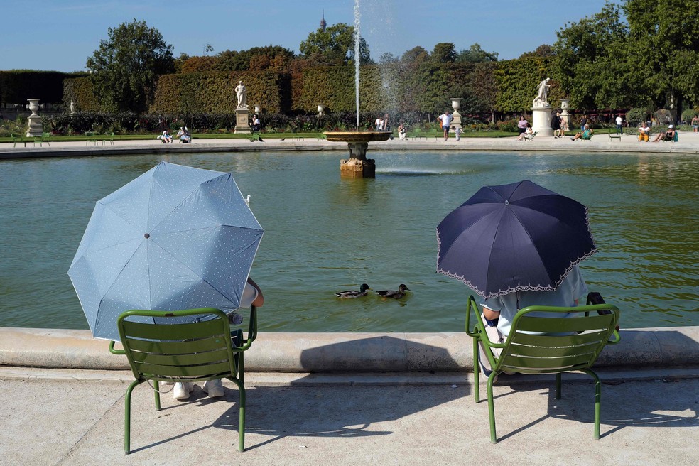 Pessoas se protegem do sol com sombrinhas em frente a fonte no jardim de Tuileries, em Paris — Foto: Valery Hache/AFP