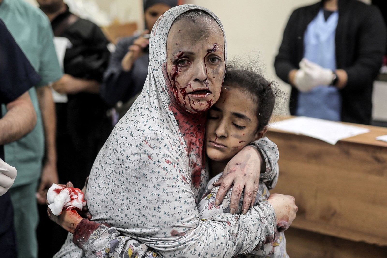 Mulher palestina ferida e coberta de poeira e sangue abraça uma menina também ferida no hospital após o bombardeio israelense de Khan Yunis, no sul da Faixa de Gaza, em 15 de novembro de 2023 — Foto: Belal KHALED / AFP