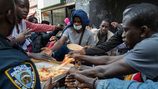 Um policial distribui pizza a dezenas de imigrantes recém-chegados à cidade de Nova York enquanto acampam do lado de fora do Hotel Roosevelt — Foto: SPENCER PLATT / Getty Images via AFP