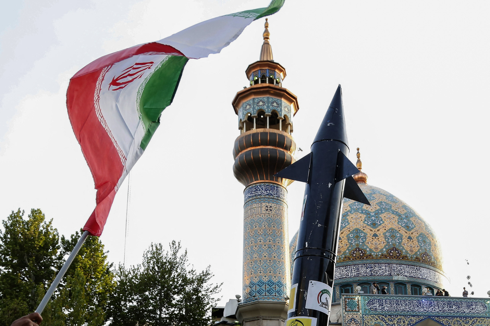 Iranianos levantam uma bandeira e a simulação de um míssil durante uma celebração após o ataque de mísseis e drones do Irã a Israel — Foto: AFP