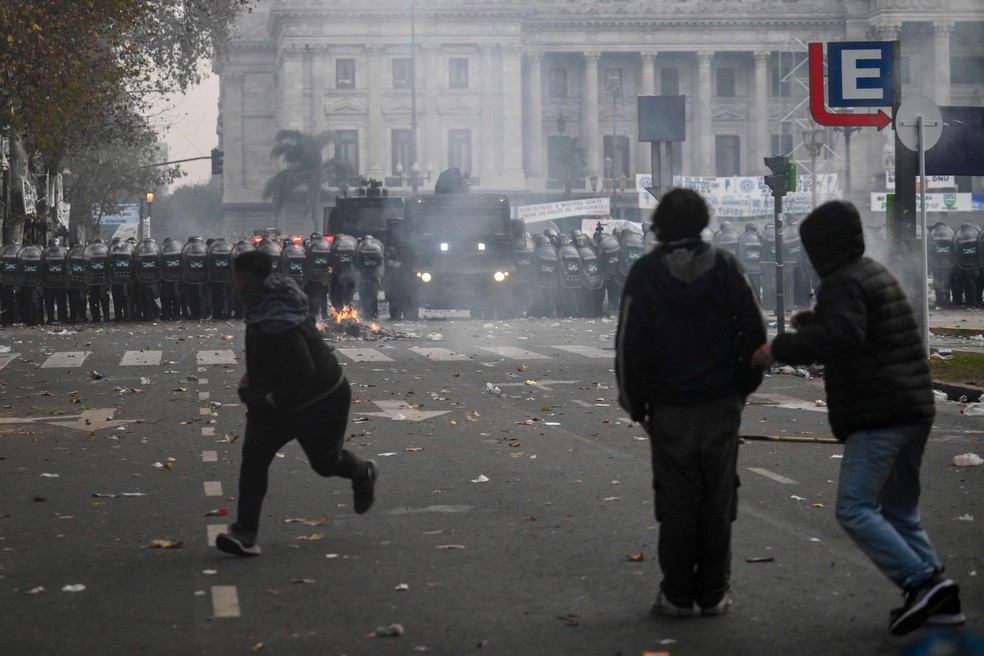 Manifestantes correm durante protesto contra a votação da Lei de Bases no Senado da Argentina — Foto: Luis ROBAYO / AFP