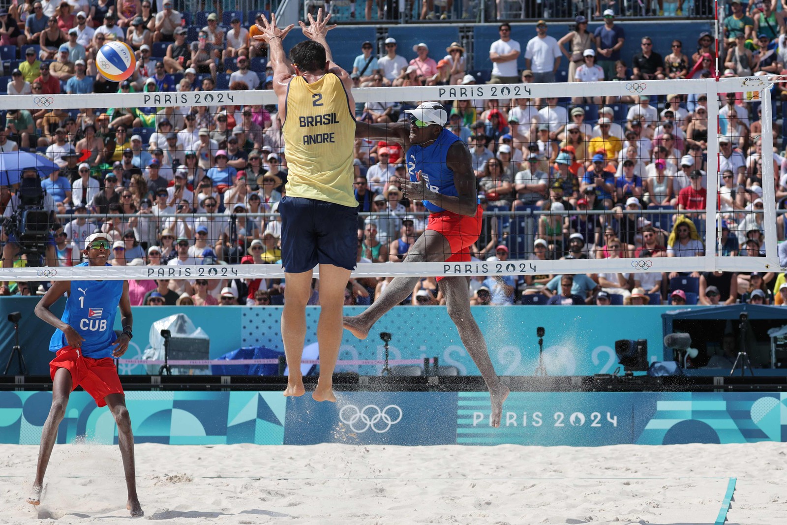 O número 02 de Cuba, Jorge Luis Alayo Moliner, chuta a bola ao lado de seu parceiro, o número 01 de Cuba, Noslen Diaz Amaro, enquanto Andre Loyola Stein, bloqueia na partida de vôlei de praia masculina da categoria D entre Brasil e Cuba durante os Jogos Olímpicos de Paris 2024, no Estádio da Torre Eiffel, em Paris, em 30 de julho de 2024 — Foto: Thomas SAMSON / AFP