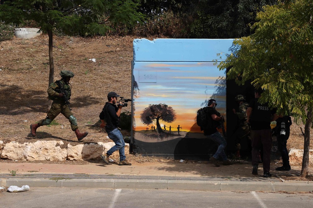 Forças de segurança e jornalistas se protegem durante um ataque com foguetes da Faixa de Gaza, na cidade de Sderot em Israel — Foto: JACK GUEZ/AFP