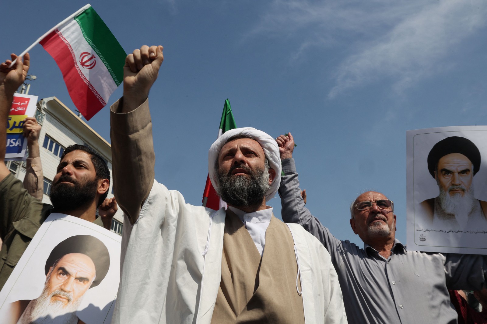 Clérigo, muçulmano xiita, iraniano levanta o punho cerrado enquanto outros carregam fotos do falecido líder supremo do Irã, Ruhollah Khomeini, durante manifestação anti-Israel - Foto: Atta KENARE / AFP