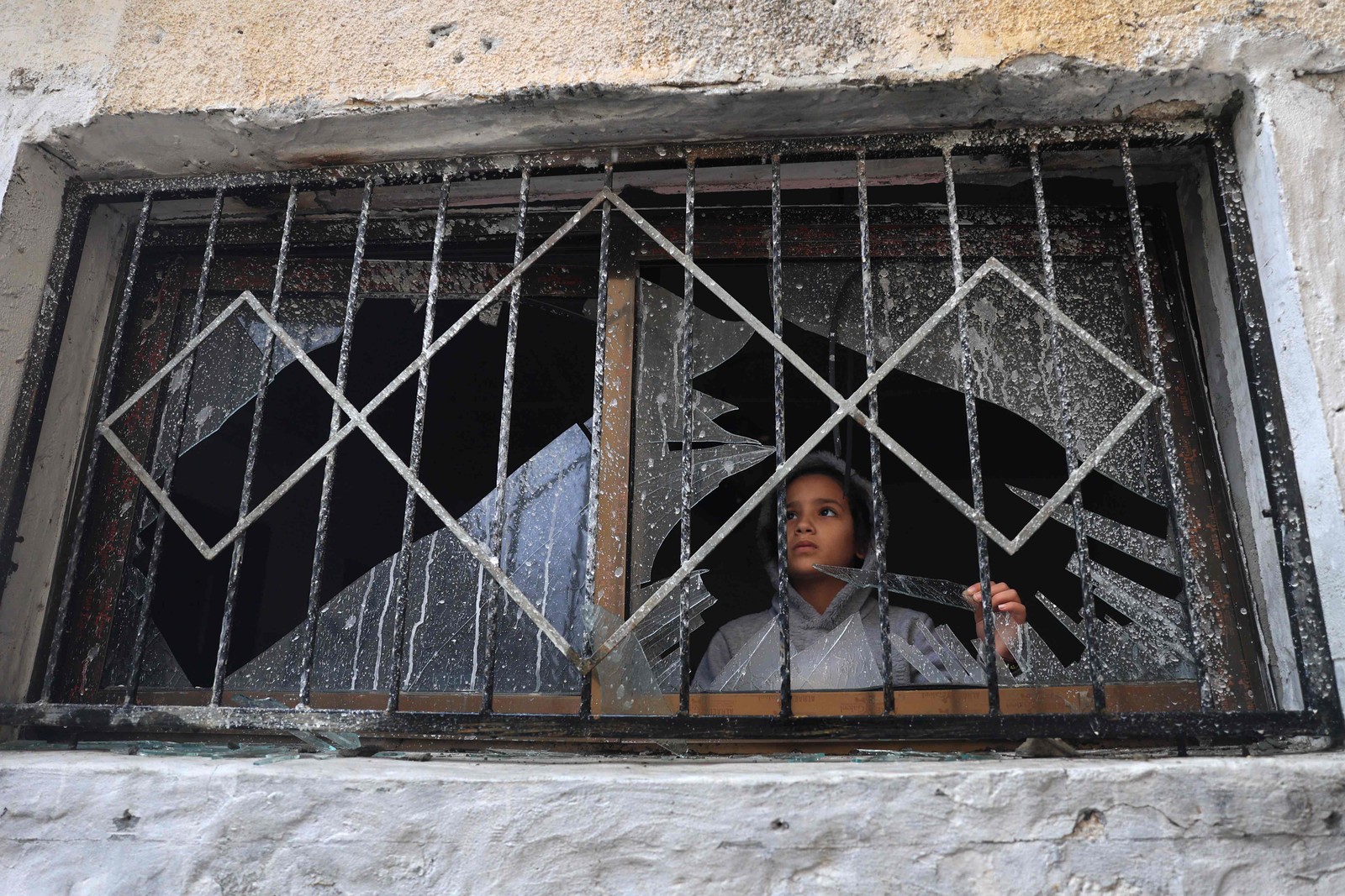 Uma criança palestina olha pelo vidro quebrado de uma janela, destruída durante bombardeios israelenses, em Rafah, no sul da Faixa de Gaza — Foto: SAID KHATIB / AFP