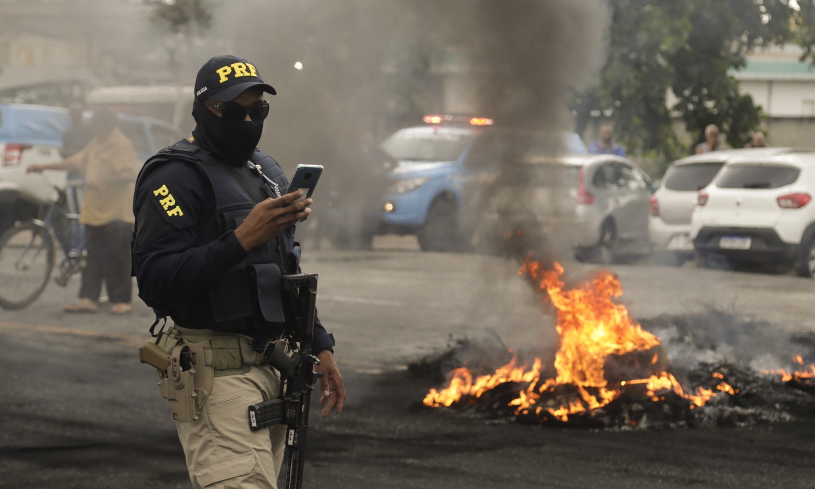 Agente da Polícia Rodoviária Federal manuseia celular ao lado de barricada de fogo na BR-101, na altura de Itaboraí — Foto: Gabriel de Paiva/Agência O Globo