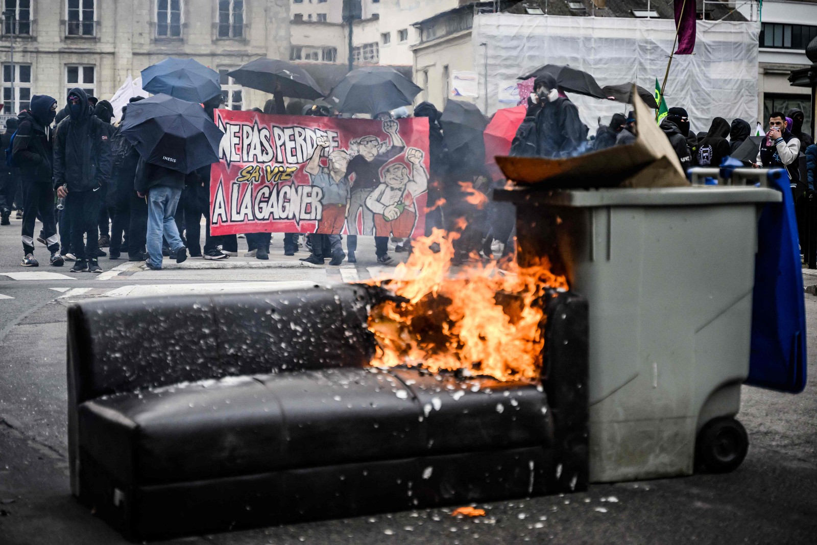 Manifestantes seguram uma faixa perto de um barricada em chamas  — Foto: LOIC VENANCE / AFP