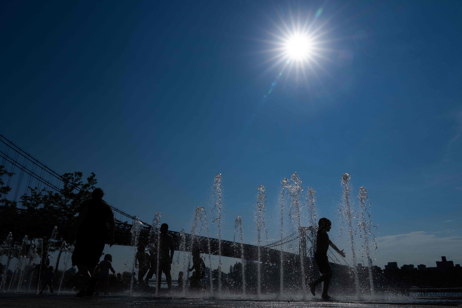 Pessoas brincam em uma fonte de água no Domino Park, no Brooklyn, Nova York, enquanto uma onda de calor atinge o nordeste dos EUA — Foto: Adam GRAY / AFP