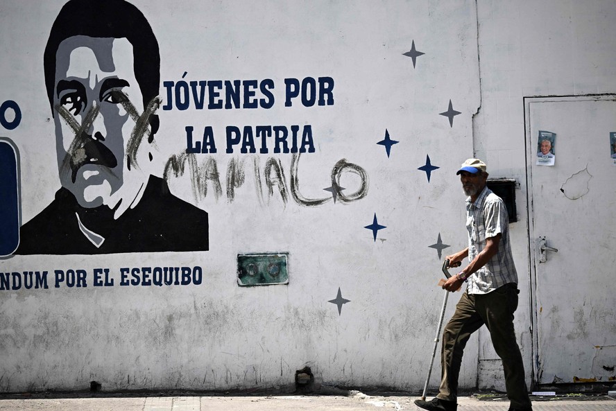 Homem caminha perto de mural representando o presidente da Venezuela, Nicolás Maduro, em Caracas