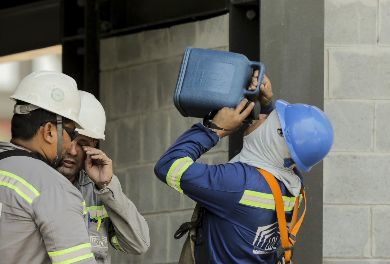 Operários tomam galões de água e usam equipamento para se proteger do sol — Foto: Gabriel de Paiva/Agência O Globo