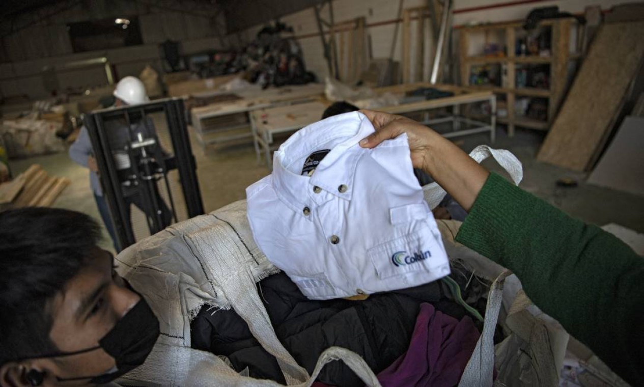 Homens trabalham em uma fábrica que recicla roupas usadas descartadas no deserto do Atacama para painéis de madeira para isolamento de paredes de habitações sociais, em Alto Hospicio, Iquique, Chile  — Foto: MARTIN BERNETTI / AFP