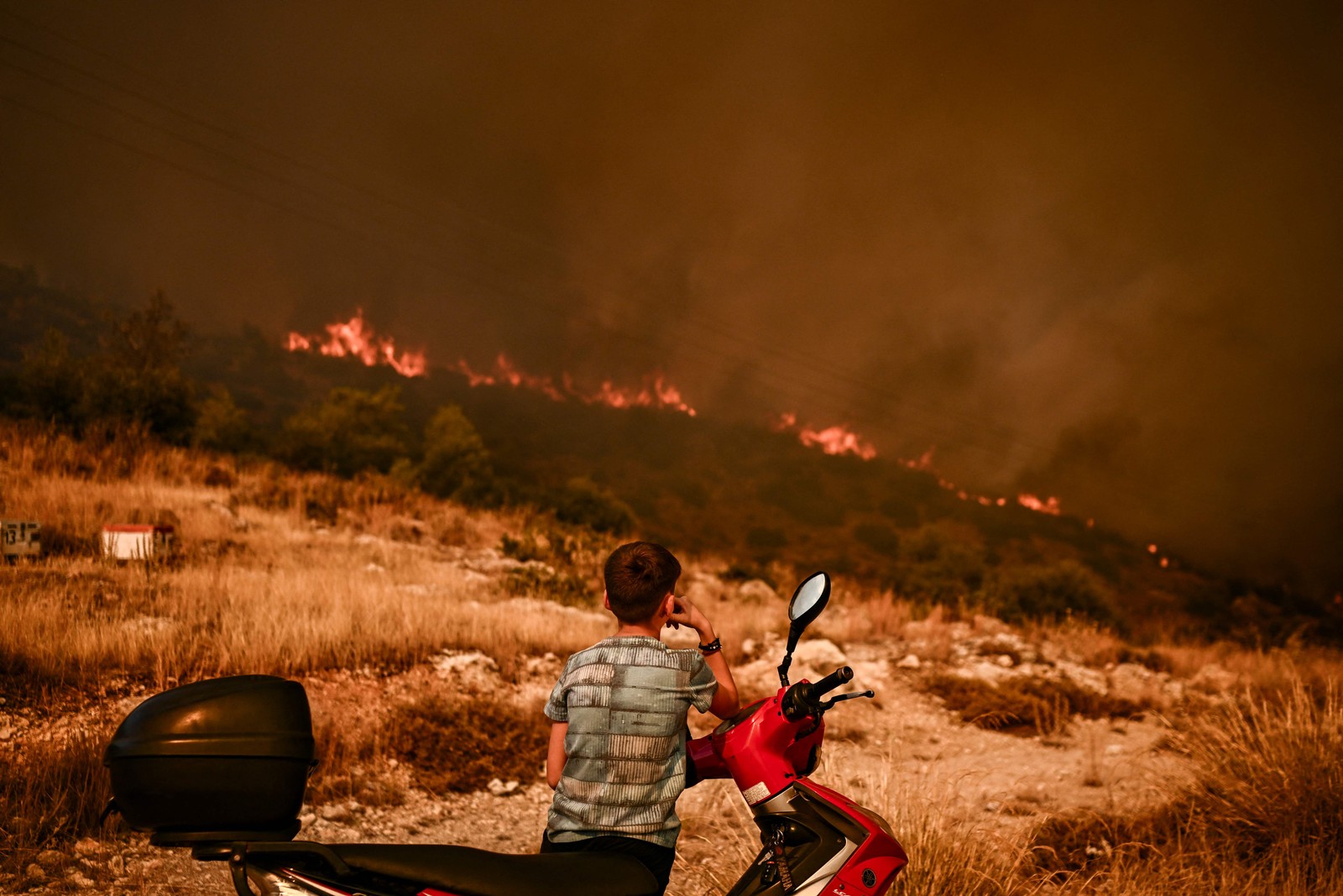 Menino observa um incêndio florestal em Chasia, nos arredores de Atenas, em 22 de agosto de 2023. — Foto: Angelos Tzortzinis / AFP