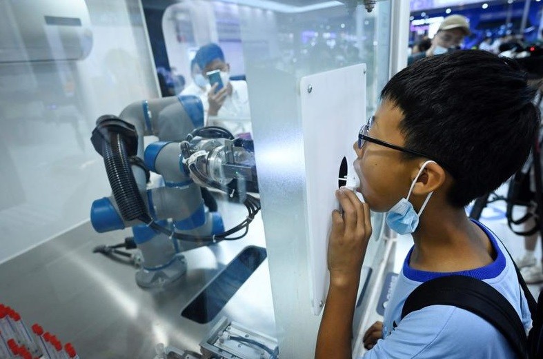 Menino faz um teste de PCR realizado por um simulação por um braço robótico durante a Conferência Mundial de Robôs, que acontece em Pequim, na China — Foto: WANG Zhao / AFP