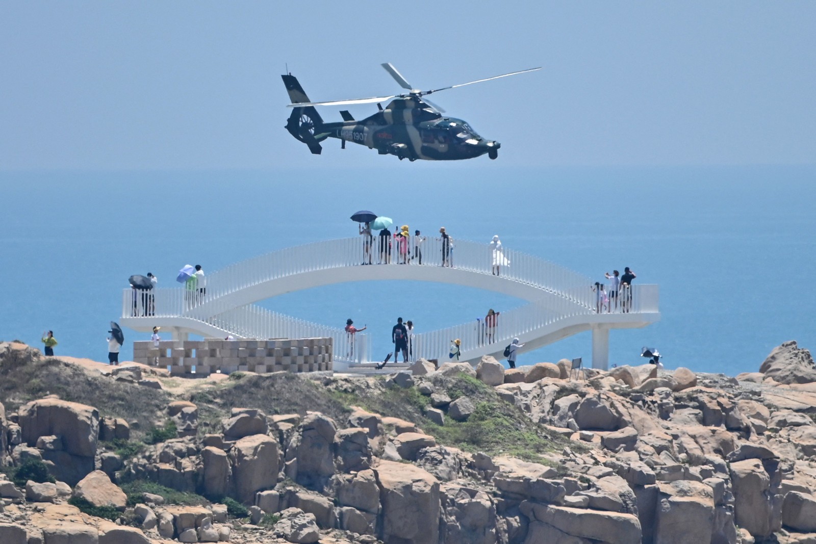 Turistas presenciam helicópteros militares chineses sobrevoam a Ilha de Pingtan, na província de Fujian, um dos pontos do litoral chinês mais próximos de Taiwan — Foto: HECTOR RETAMAL / AFP