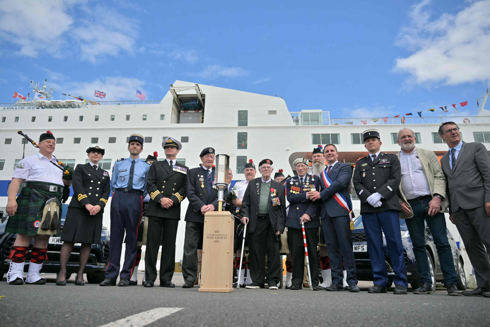 Os veteranos do Reino Unido, Stan Ford, Jim Grant (no centro), Alec Penstone  e autoridades posam com a Tocha de Comemoração da organização Graves de guerra da Commonwealth na estação Brittany Ferries, em Ouistreham, noroeste da França, em 4 de junho de 2024 — Foto: Lou Benoist / AFP